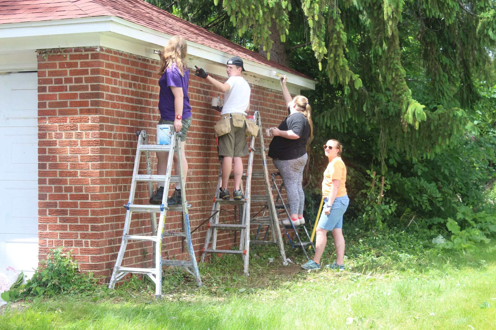 Community members stand on ladders helping to paint the exterior of a house with the Schoolcraft Improvement Association